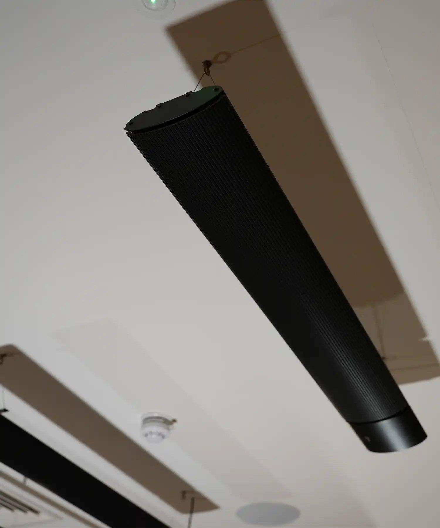 Close-up of a suspended IKON infrared heater bar mounted to the ceiling, showcasing its slim cylindrical design and discreet installation.