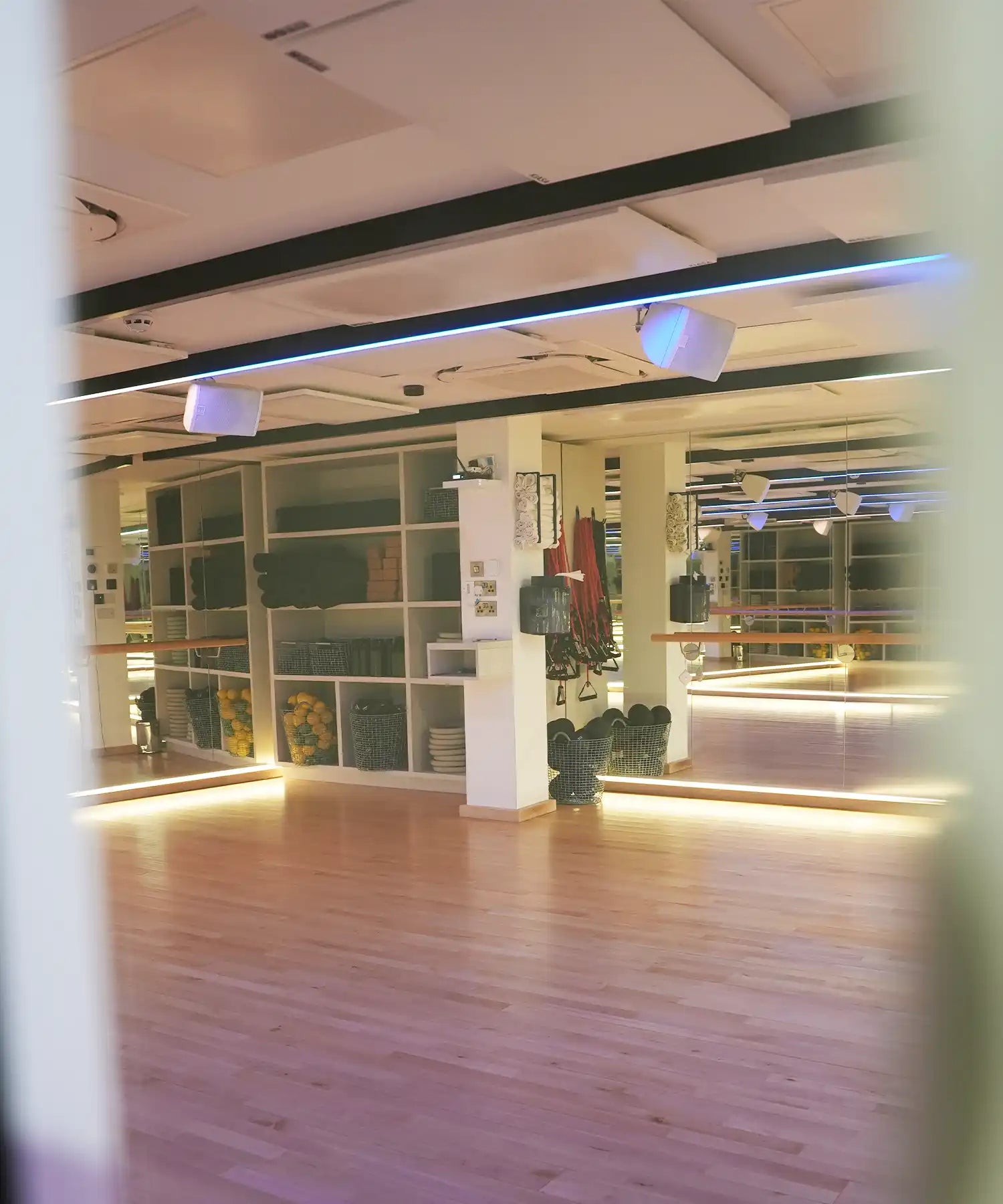 Contemporary yoga studio with mirrored walls, organised props, wooden flooring, and ceiling-mounted IKON infrared heater bars delivering consistent radiant warmth.