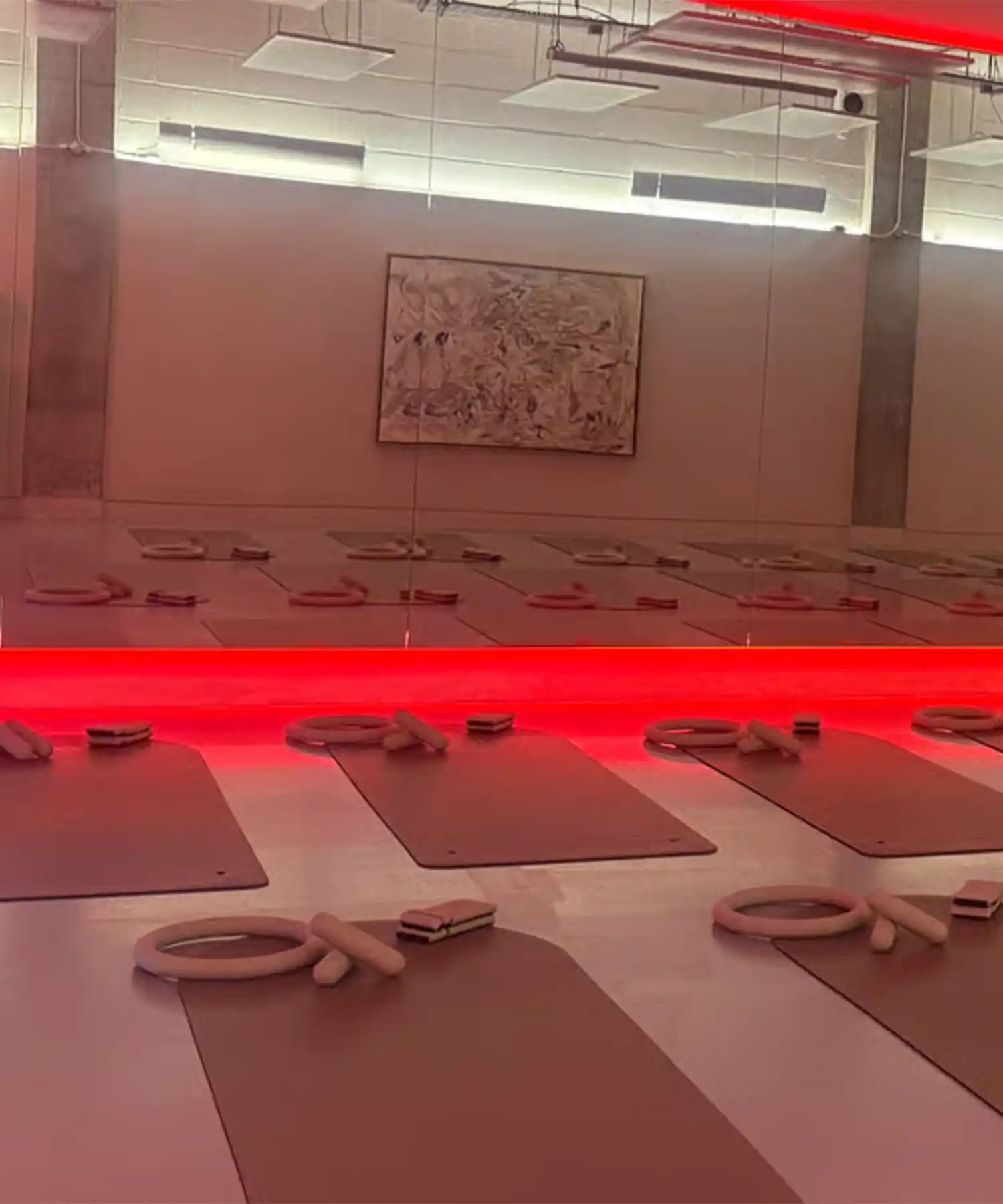 Wide view of YOURS Studio London class zone with hanging infrared heating panels above, neat rows of mats and studio ambient red lighting.