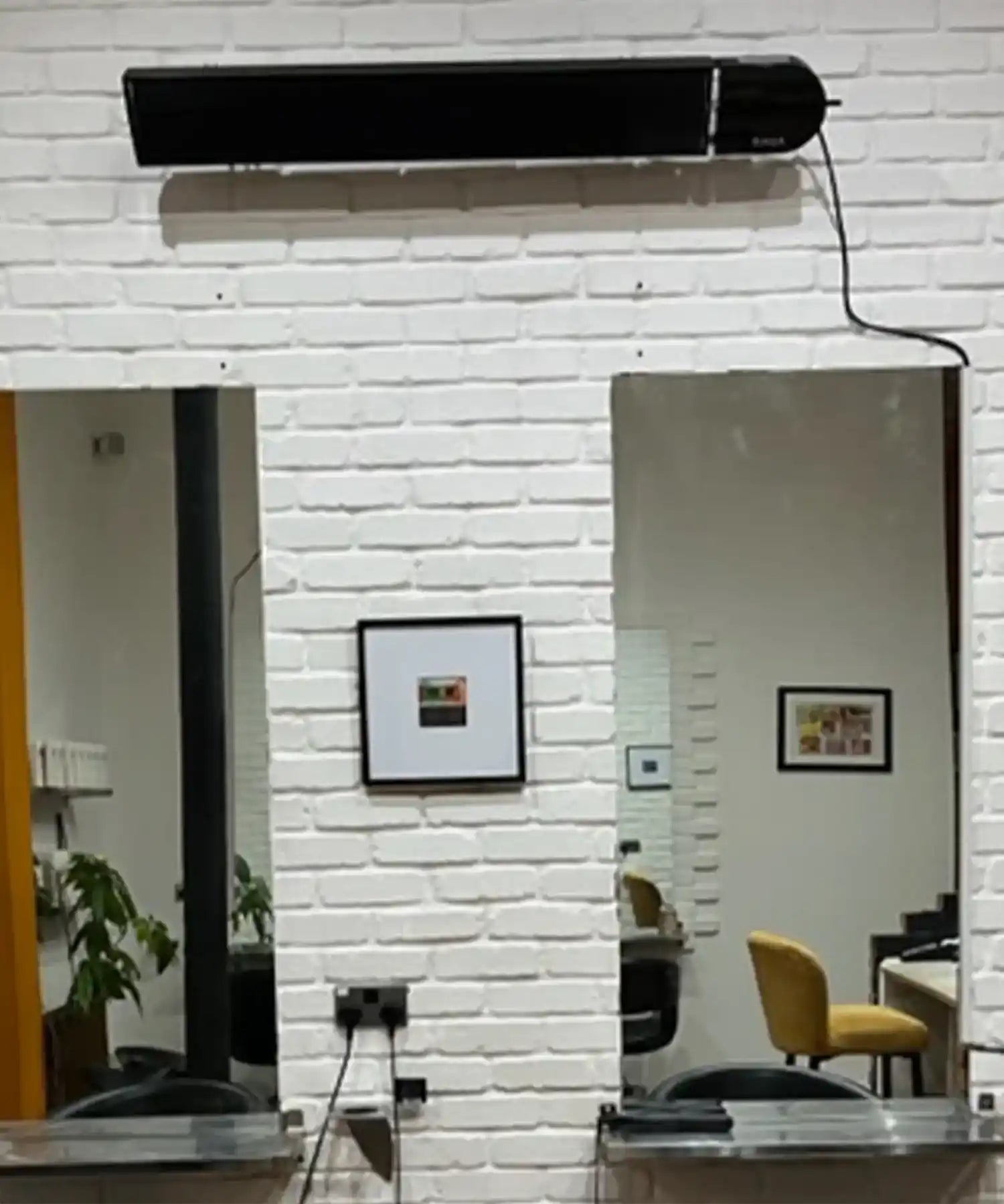 Black KIASA Heater Bar mounted on a white painted brick wall between two mirrors in a salon or barbershop interior.
