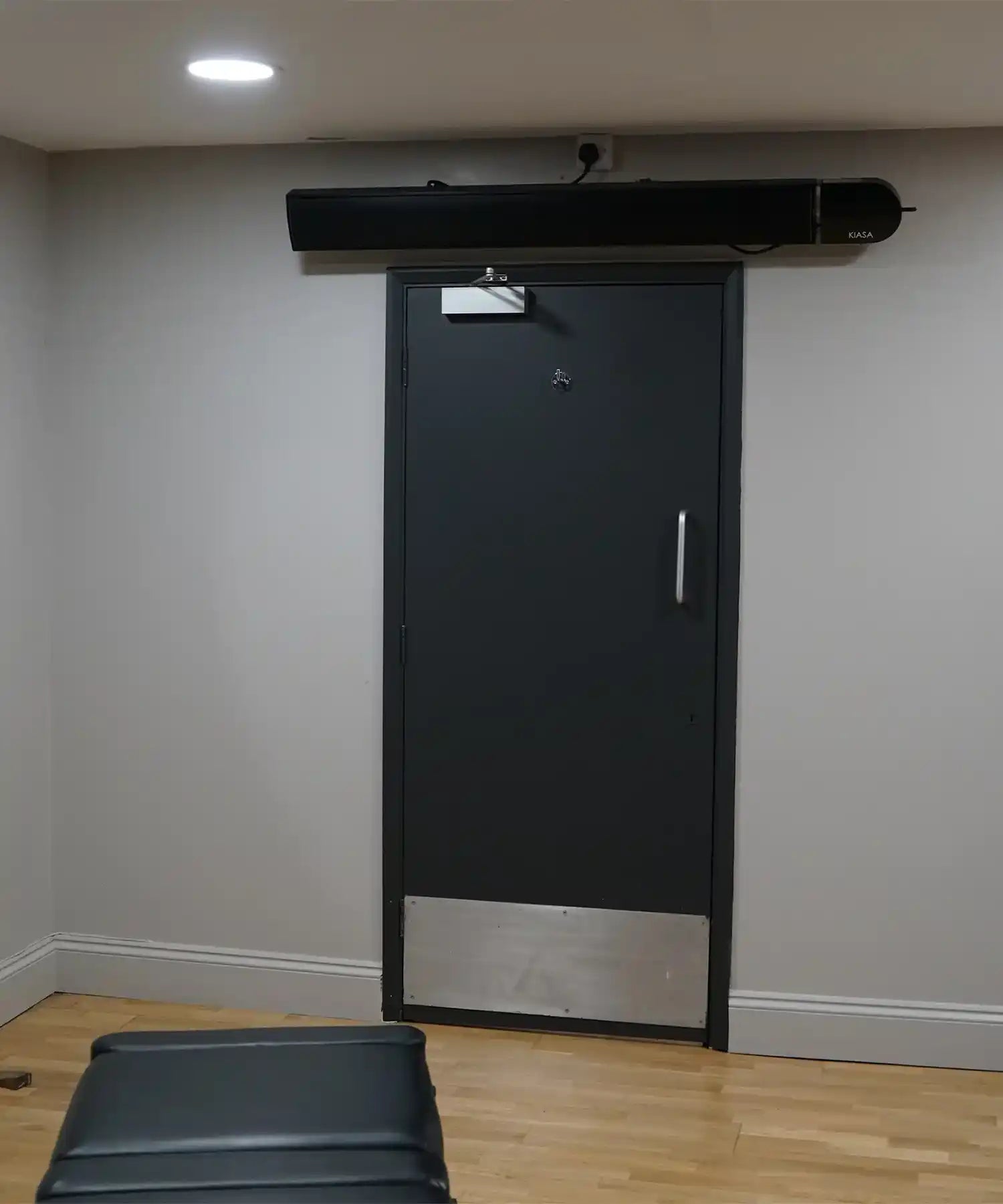 KIASA black infrared heater bar mounted above a doorway in a commercial space with gym flooring and neutral walls.