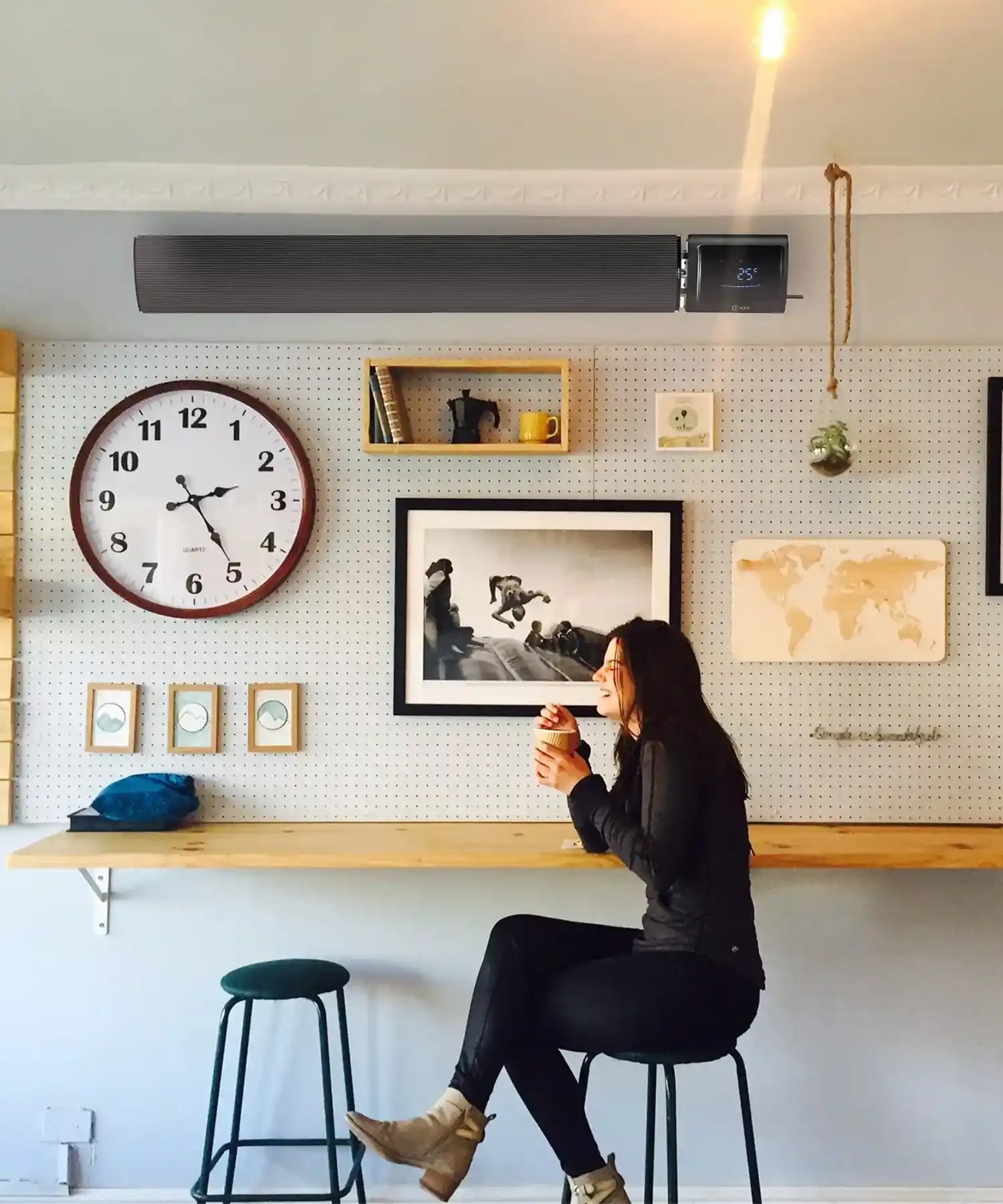Black Kiasa IKON infrared heater wall mounted in a trendy café above a woman enjoying coffee.