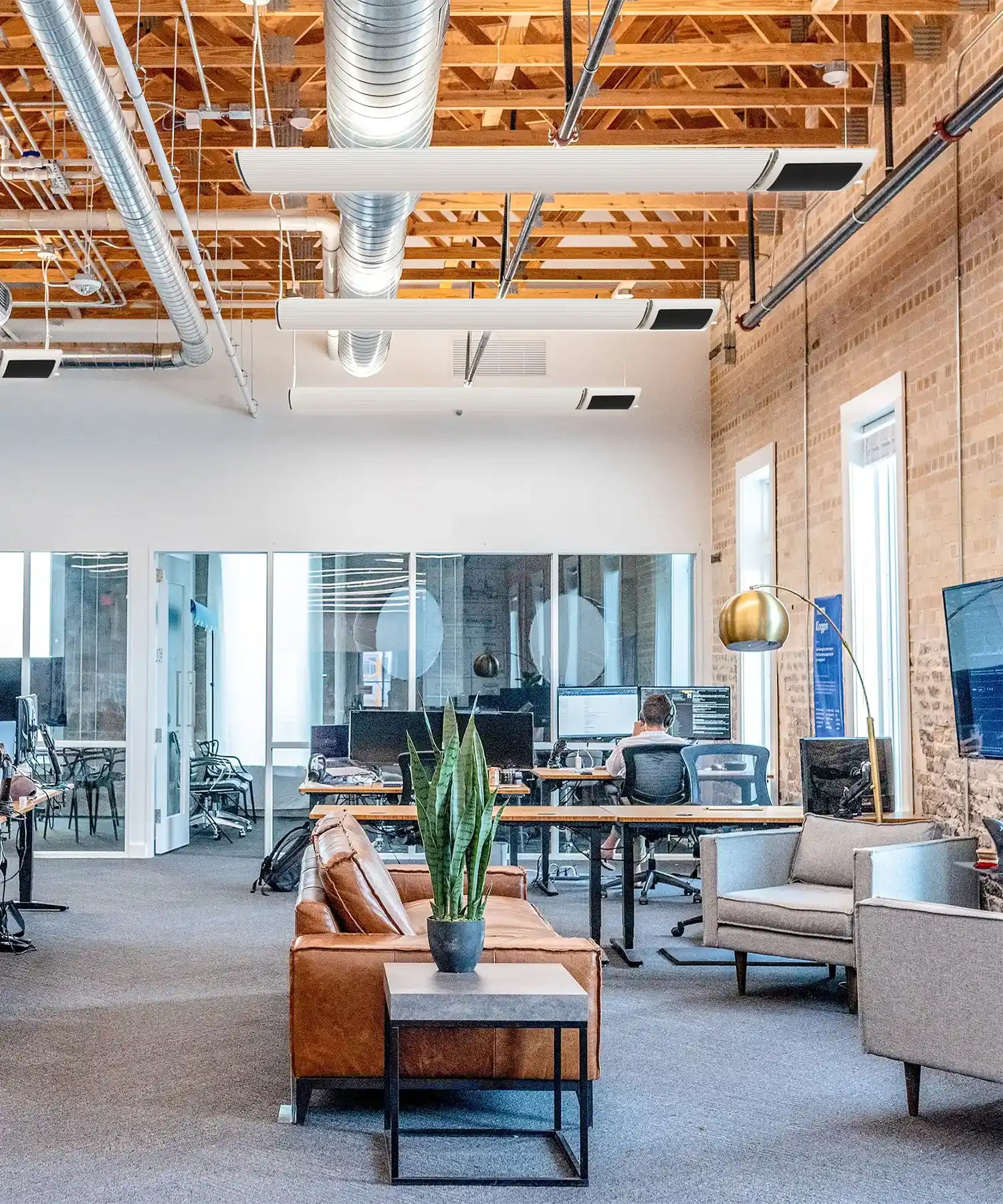 White Kiasa IKON infrared heaters suspended from an exposed ceiling in a modern industrial office space.