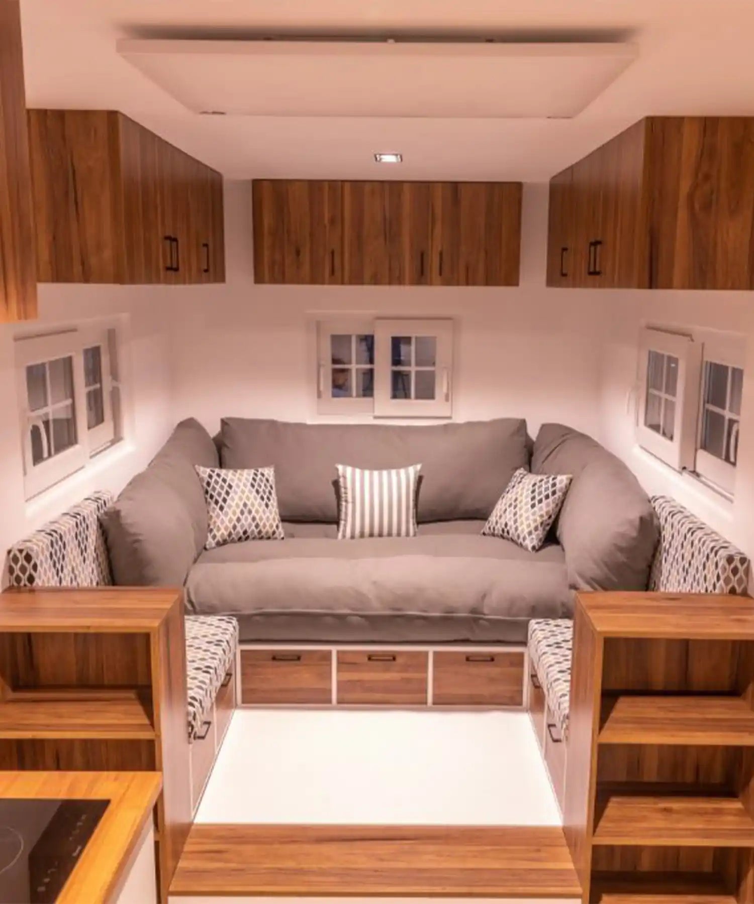Ceiling-mounted infrared panel heater in a tiny home living room with grey sofa, wooden cabinets, and modern cushions.