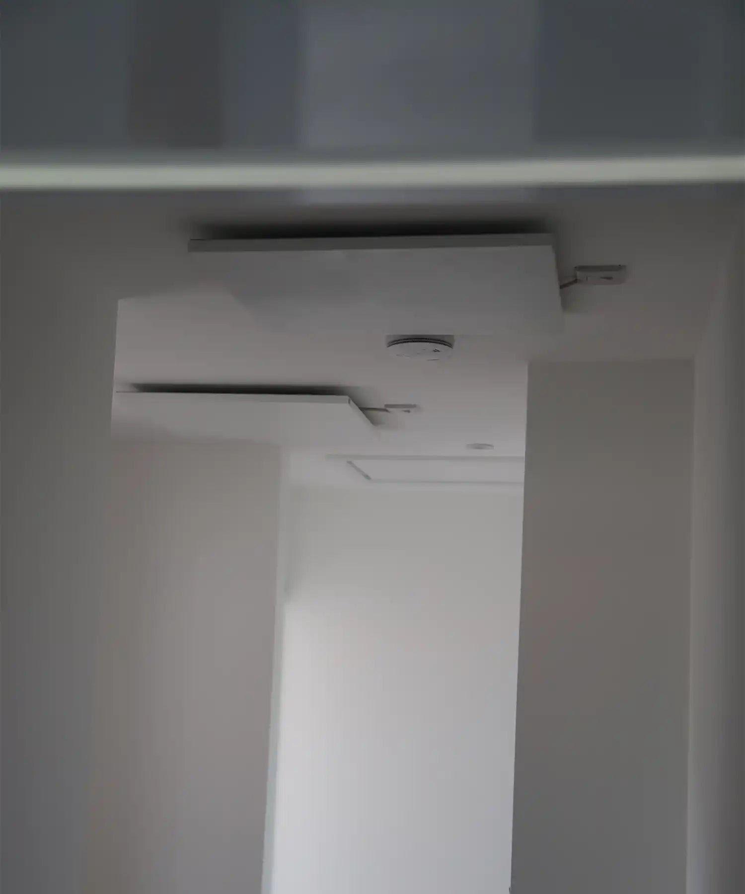Ceiling-mounted KIASA Prime infrared panels in a minimalist, white hallway with smoke detectors and recessed lighting.