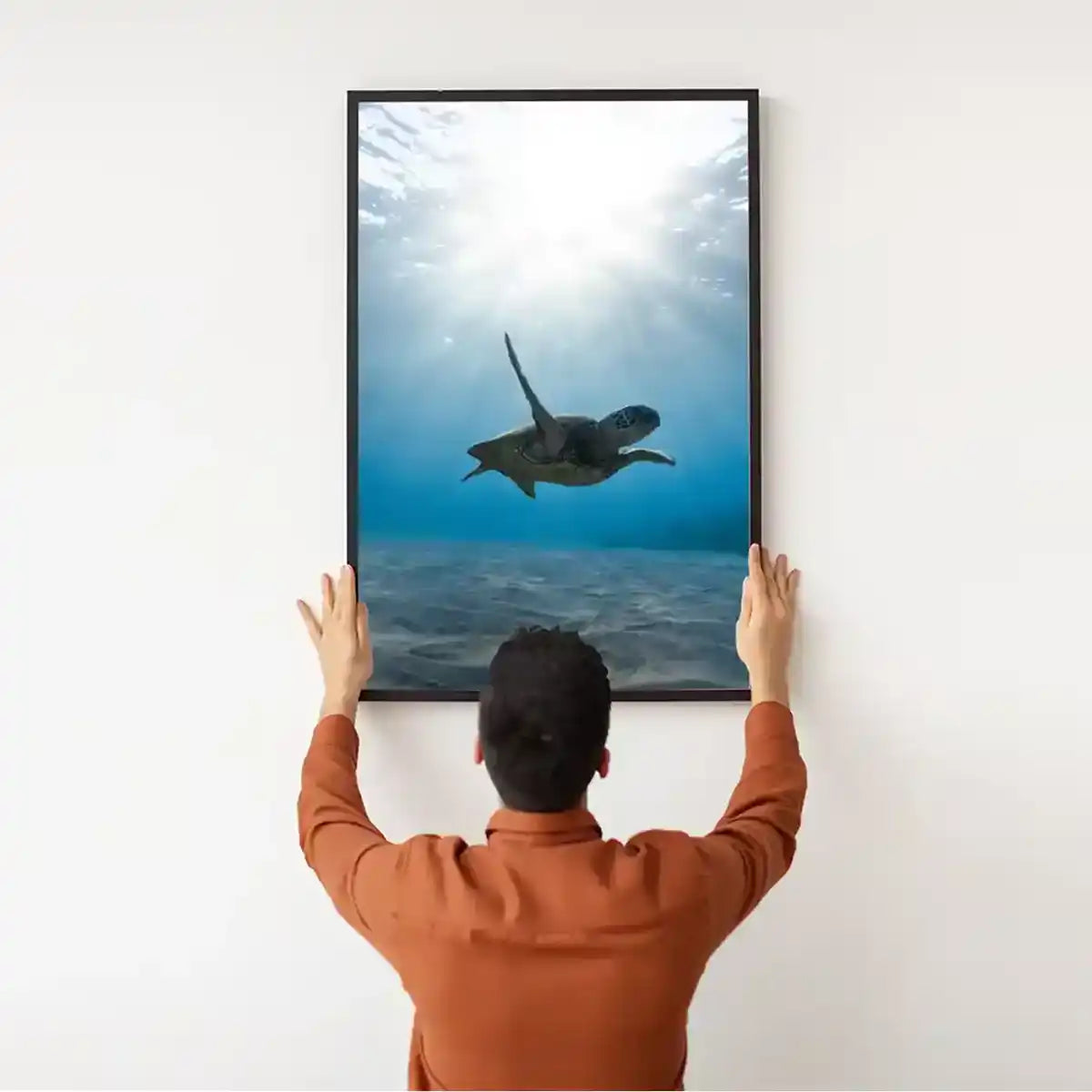 Man installing a framed turtle ocean print infrared picture heater onto a plain white wall.