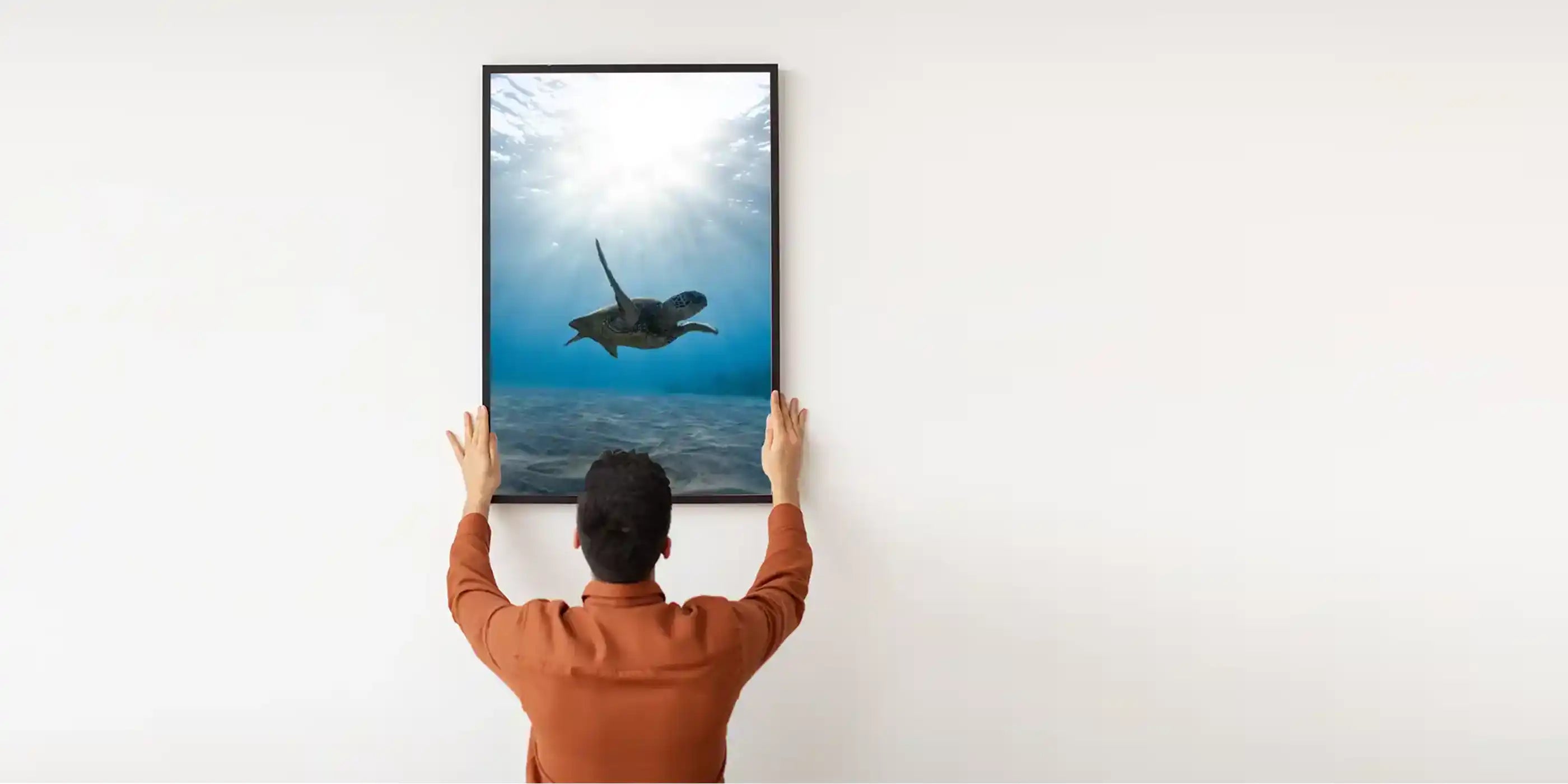 Man installing a framed turtle ocean print infrared picture heater onto a plain white wall.