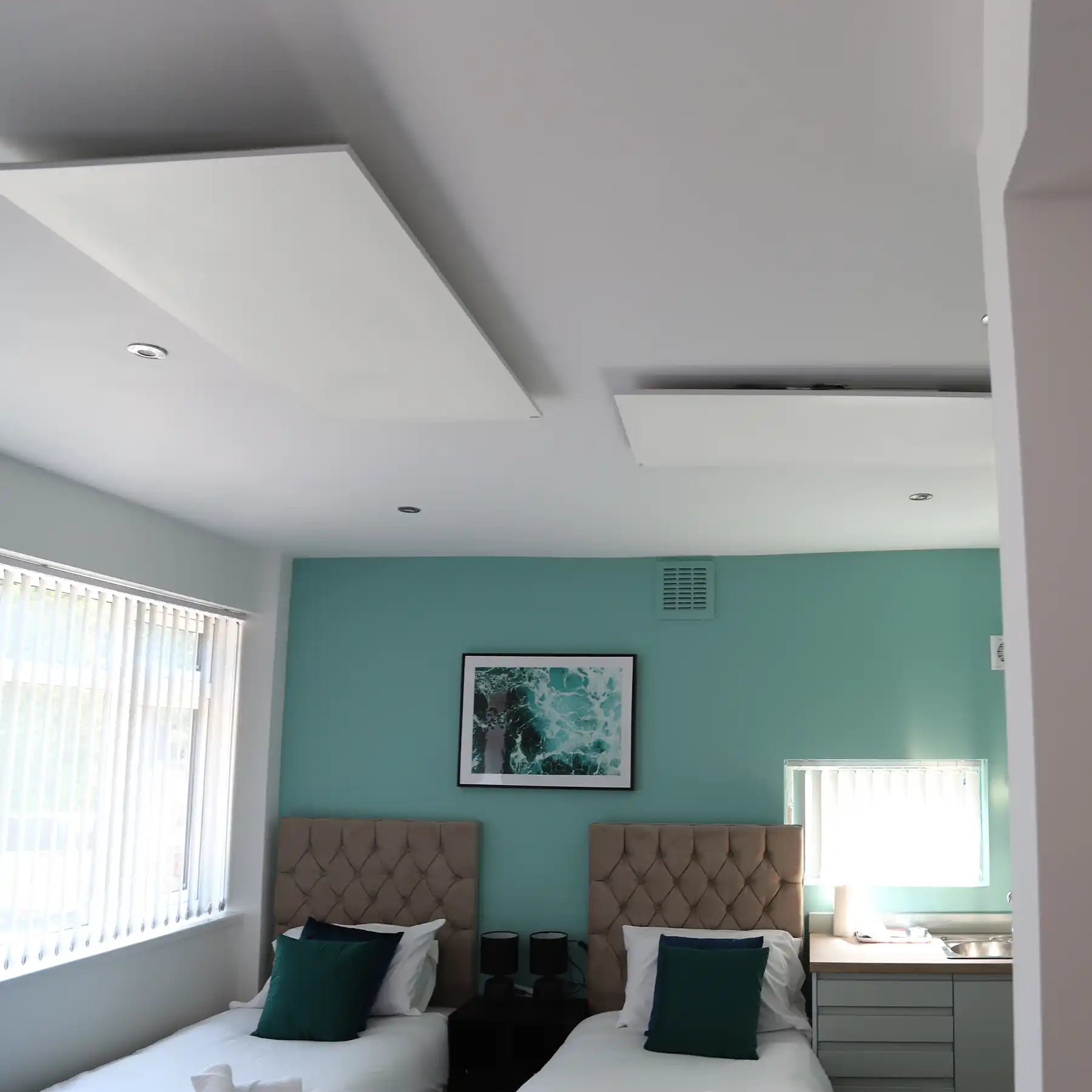 Kiasa ceiling-mounted infrared panel heaters in a guest bedroom with twin beds, teal accent wall, and modern décor.