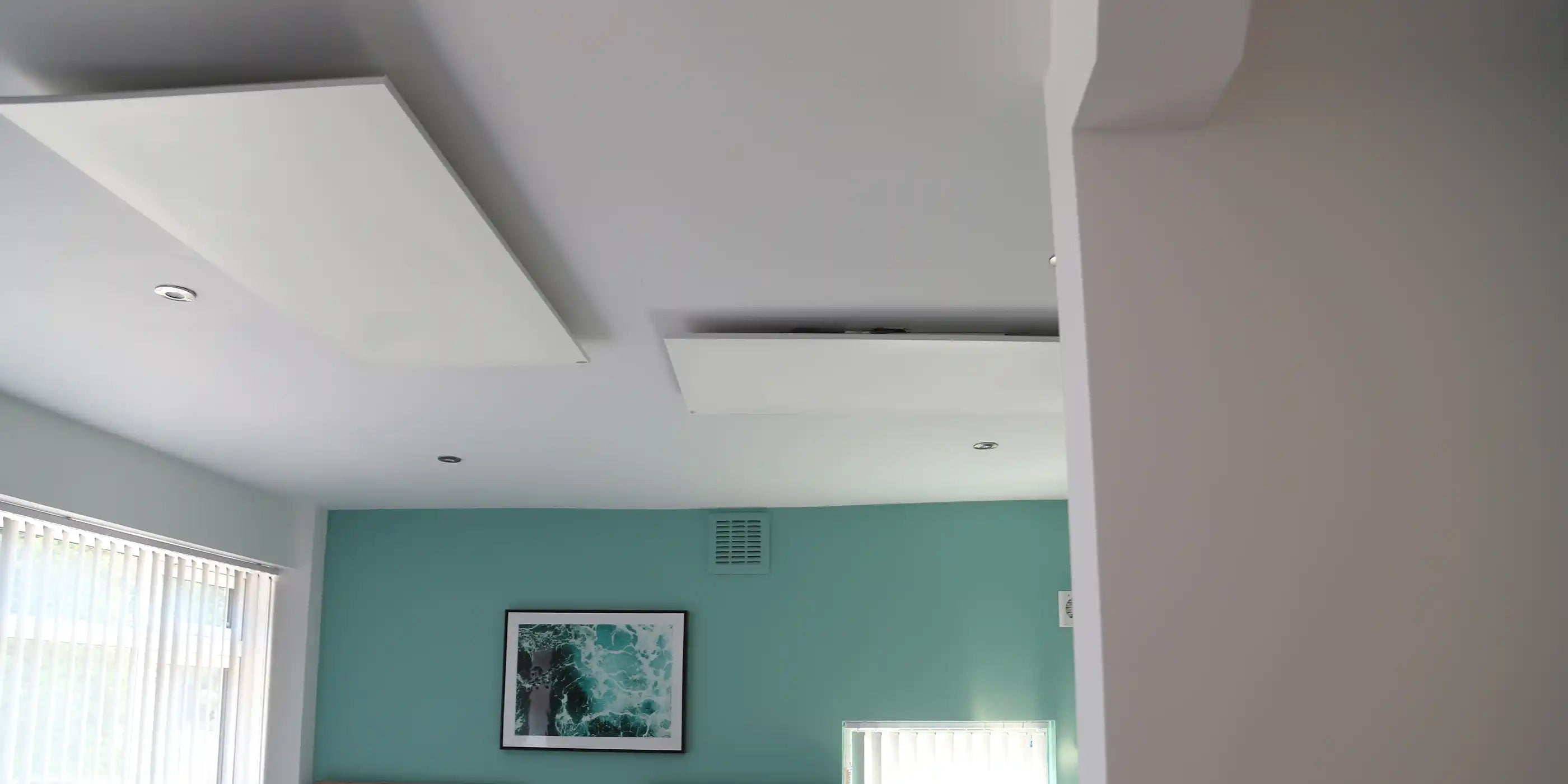 Kiasa ceiling-mounted infrared panel heaters in a guest bedroom with twin beds, teal accent wall, and modern décor.
