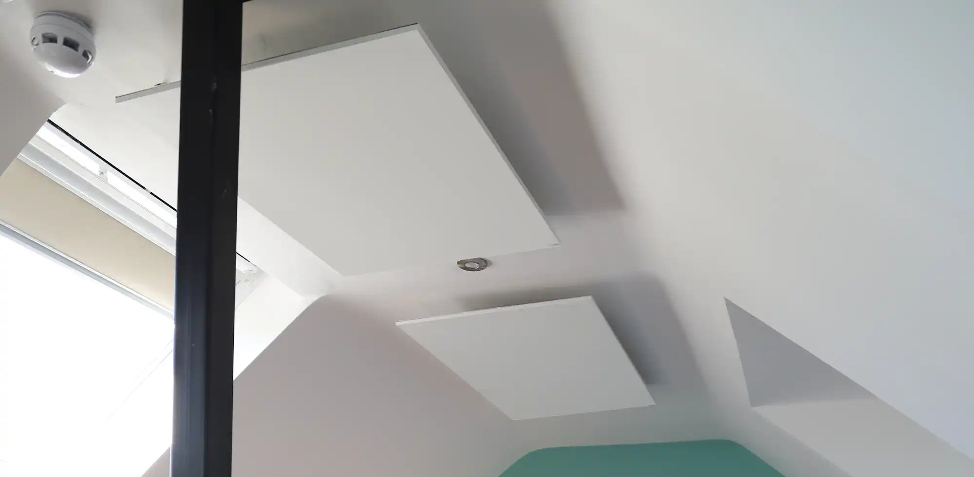 Dual Kiasa infrared ceiling panels installed on a sloped ceiling in a bright room with contemporary lighting and a skylight.