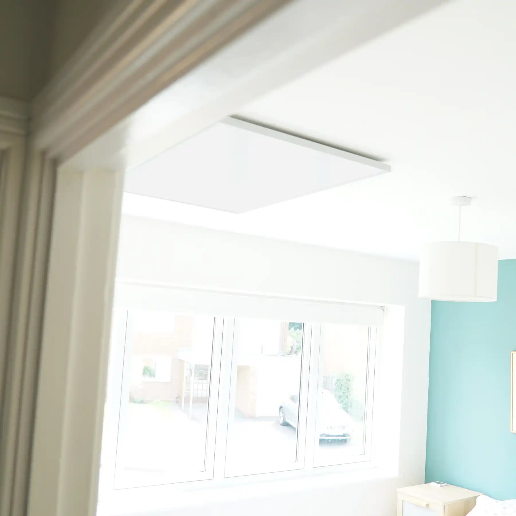 Ceiling-mounted Kiasa Classic infrared panel heater viewed from a doorway in a modern room with teal accent wall.