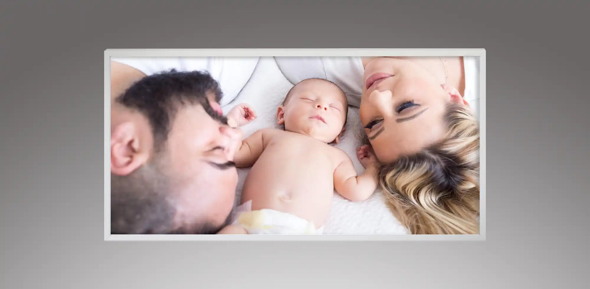 Kiasa infrared panel heater customized with a printed family photo of parents and a sleeping baby, mounted on a grey wall.