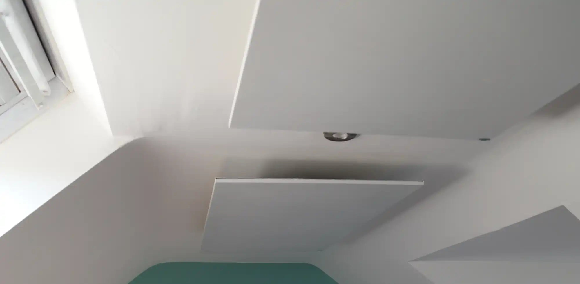 Wall-mounted Kiasa Kore infrared panel heater above a black sofa in a modern apartment with neutral tones and city view through the window.