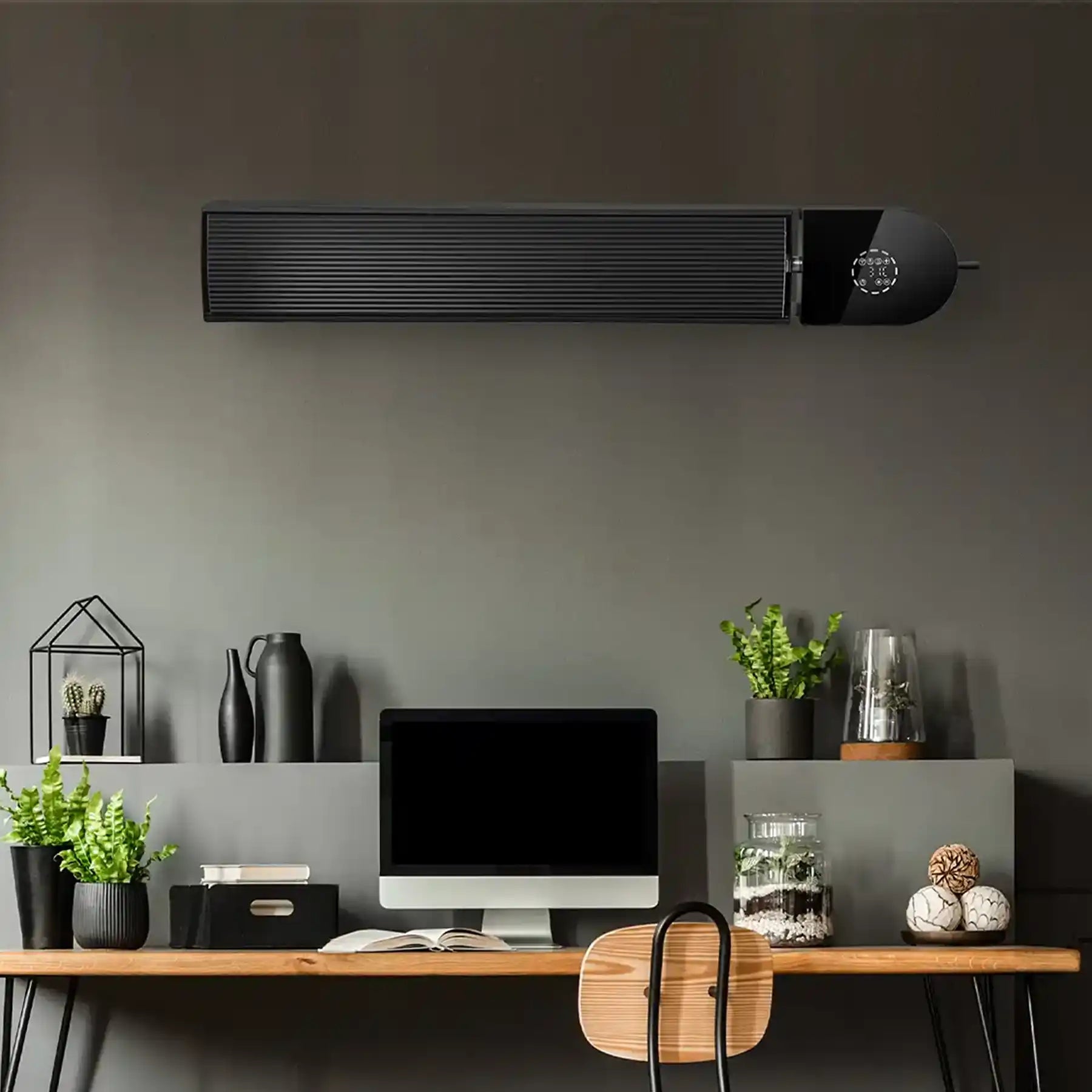 KIASA black infrared heater bar wall-mounted above a modern home office desk with plants, books, and a computer on a dark feature wall.