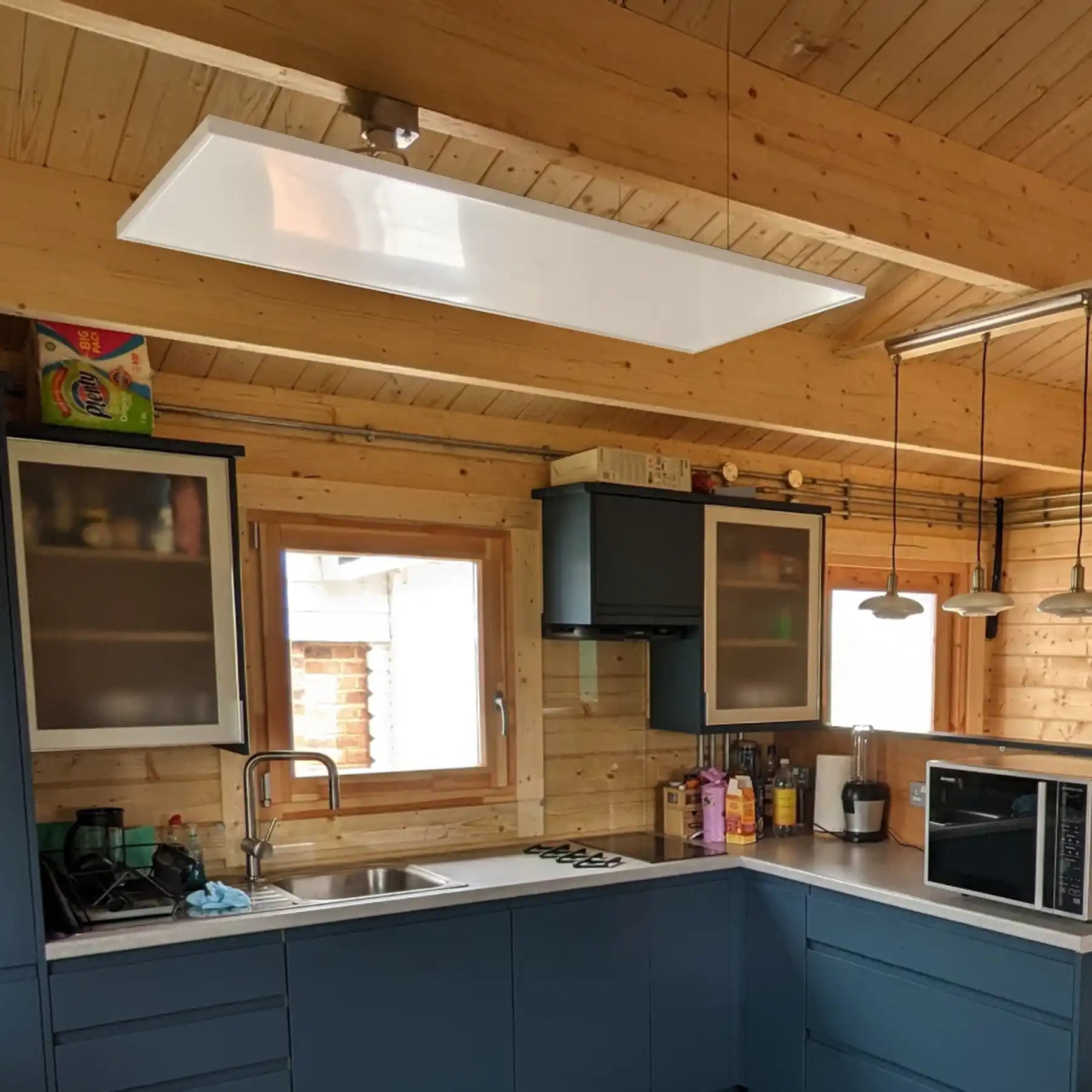 Three Kiasa Classic infrared panel heaters mounted on the ceiling of a rustic wooden kitchen interior with exposed beams.