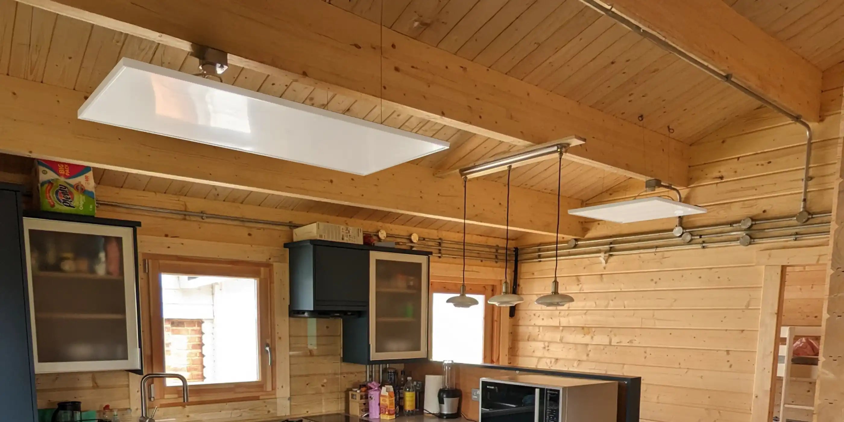 Three Kiasa Classic infrared panel heaters mounted on the ceiling of a rustic wooden kitchen interior with exposed beams.