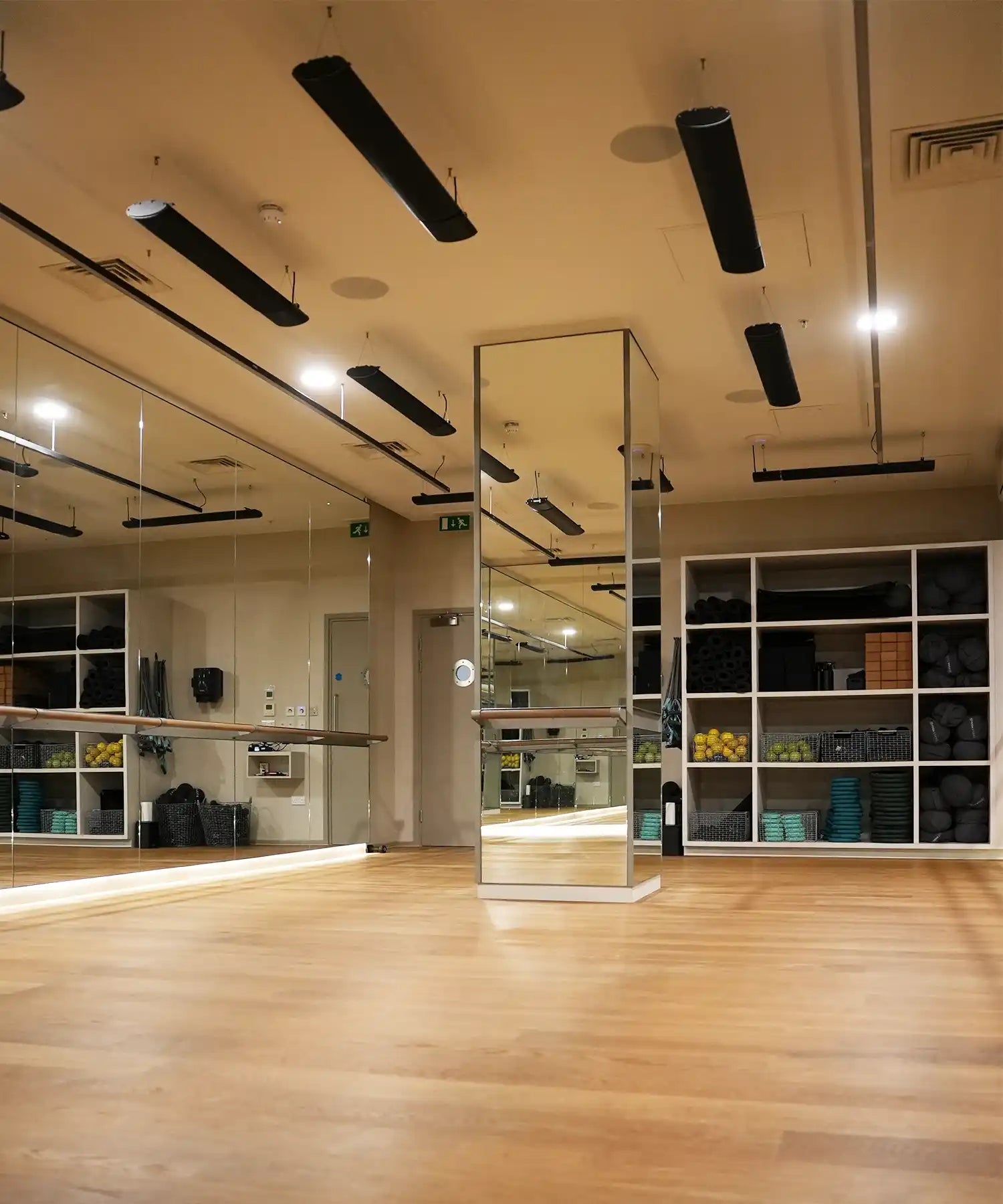 Warm-lit fitness studio with mirrored walls and ceiling-mounted IKON infrared heater bars delivering consistent, silent radiant heat for yoga and Pilates classes.