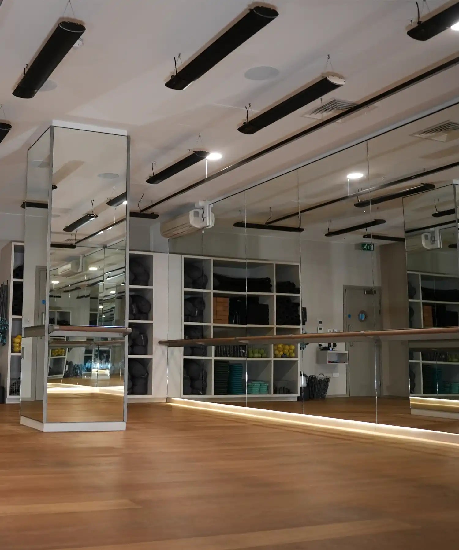 Modern mirrored fitness studio with wooden flooring and ceiling-mounted IKON infrared heater bars providing discreet, even radiant heating across the space.
