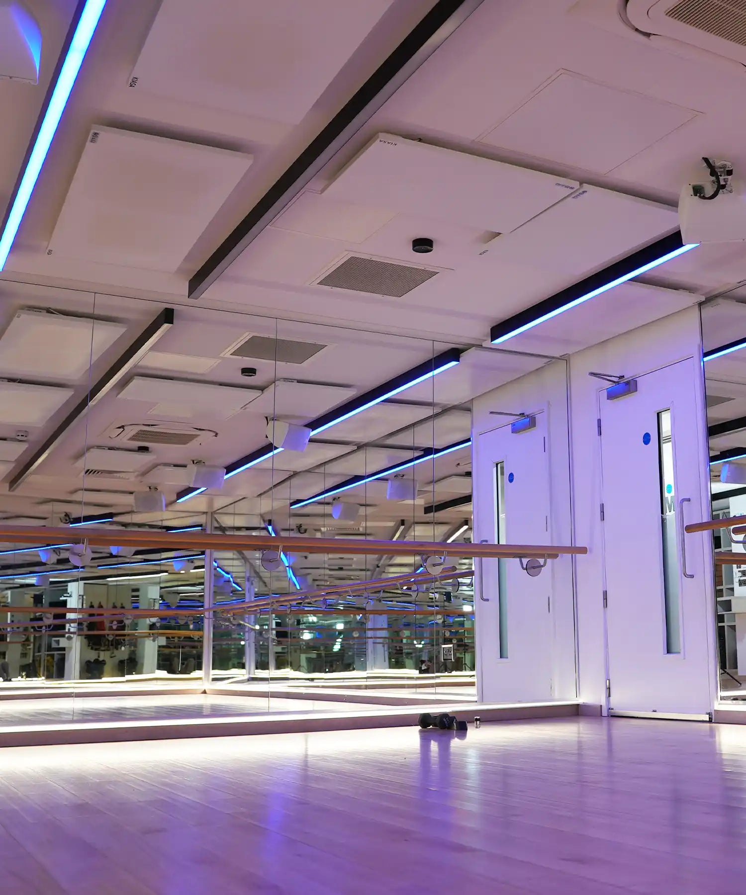 Modern fitness studio with mirrored walls, wooden flooring, ceiling-mounted infrared heating panels and IKON heater bars providing even, silent radiant heat.