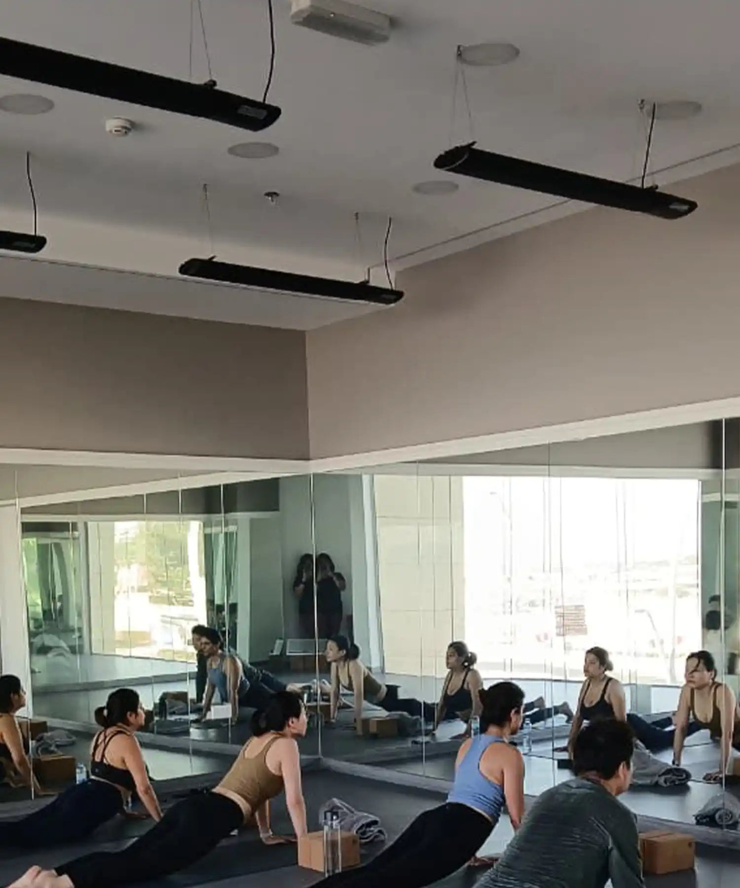 Yoga class performing upward-facing dog in a mirrored studio with ceiling-mounted infrared heater bars providing even, silent warmth throughout the space.