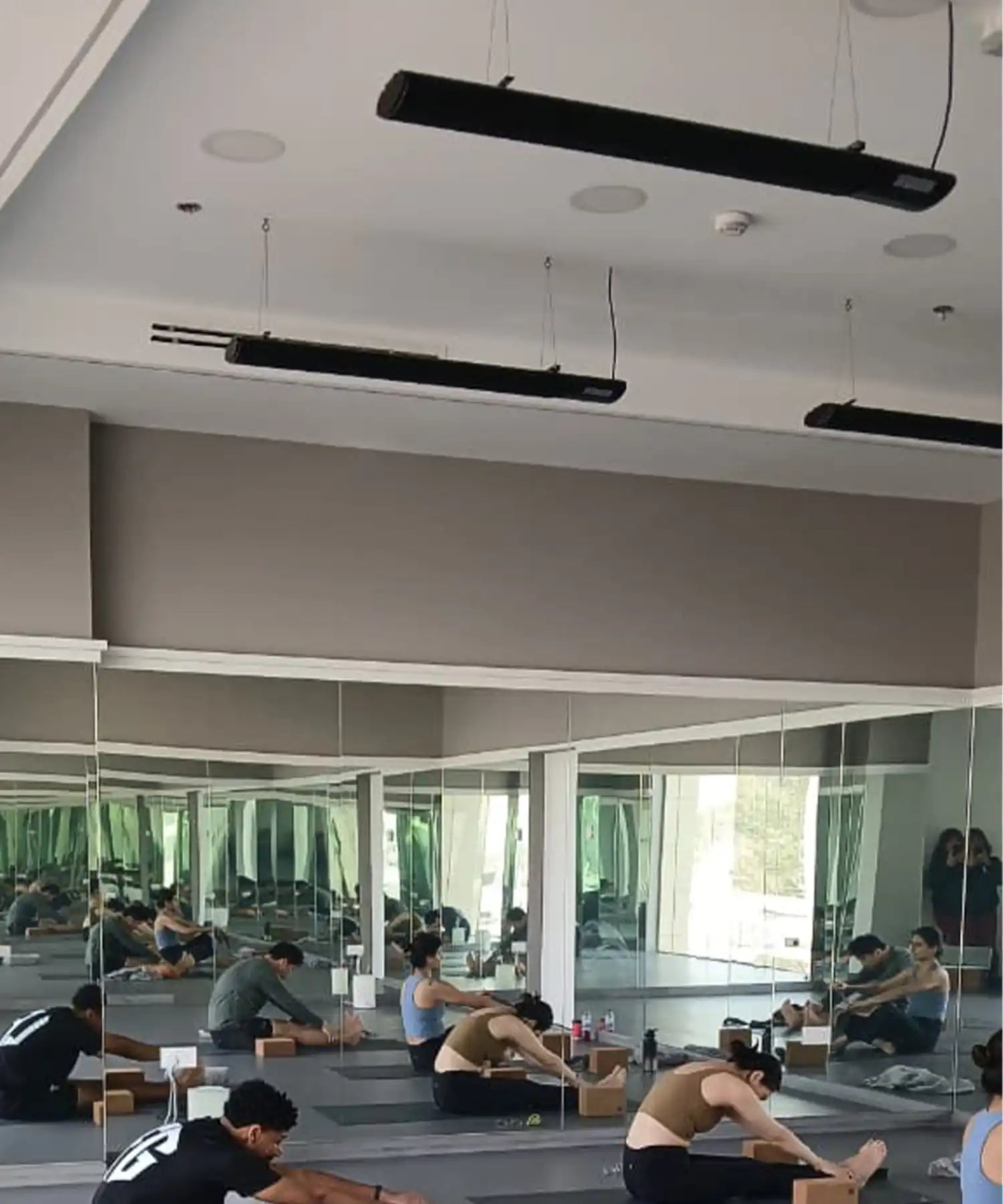 Group flexibility class in a mirrored studio with ceiling-mounted black infrared heater bars providing even, silent heat during stretching and mobility training.
