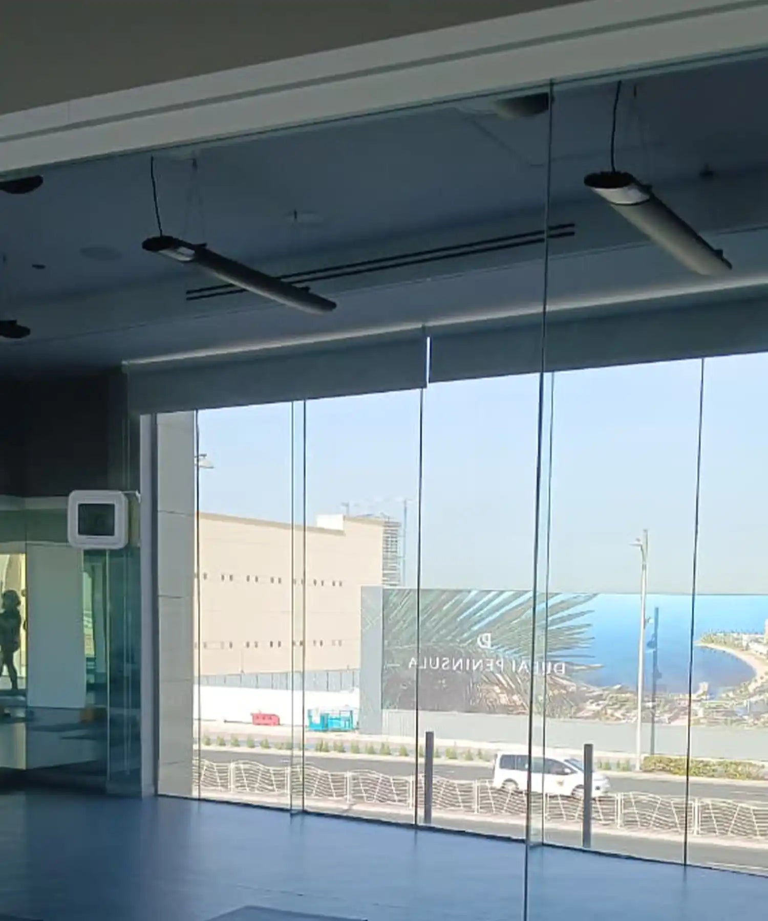 Modern fitness studio with floor-to-ceiling windows and ceiling-mounted infrared heater bars providing discreet, energy-efficient heating with a coastal view.