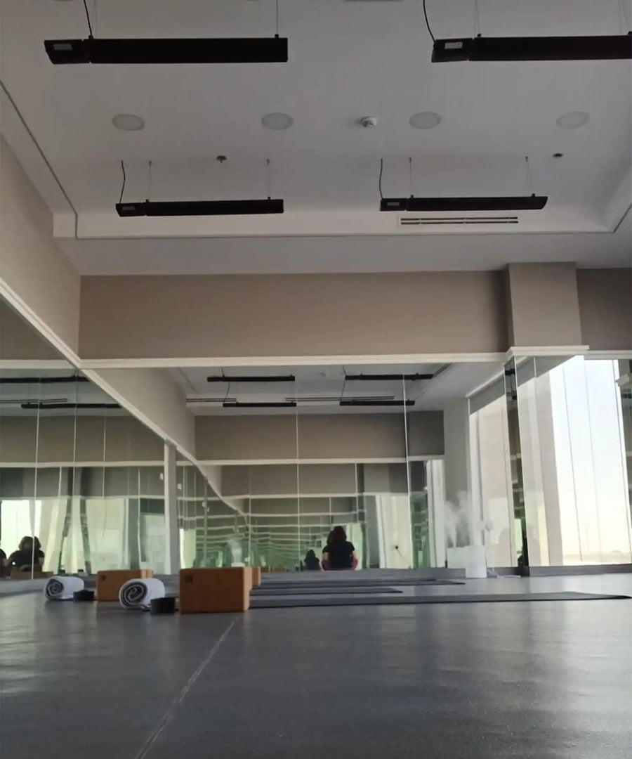 Minimalist mirrored yoga studio with ceiling-mounted black infrared heater bars providing silent, even radiant warmth for hot yoga and Pilates classes.