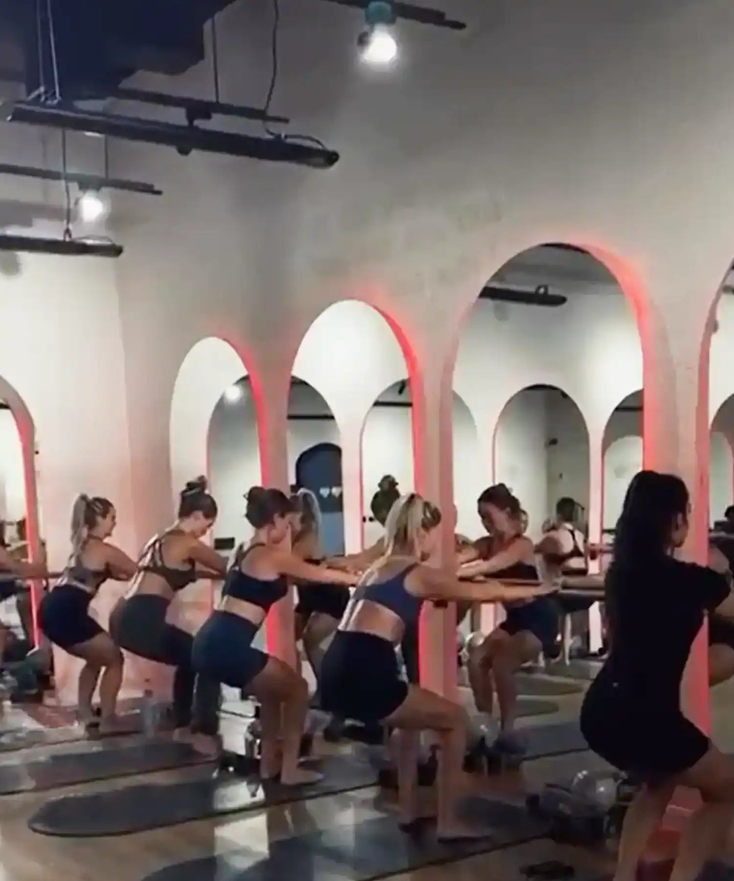 Women doing barre class in a hot-room studio at BRRN BARRE Dubai, with visible IR heater bars mounted overhead and warm ambient lighting