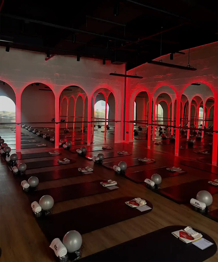 Interior of BRRN BARRE Dubai studio with rows of yoga/barre mats, red-highlighted pillars, overhead IKON infrared heater bars, and a warm-toned environment suited for hot workouts.