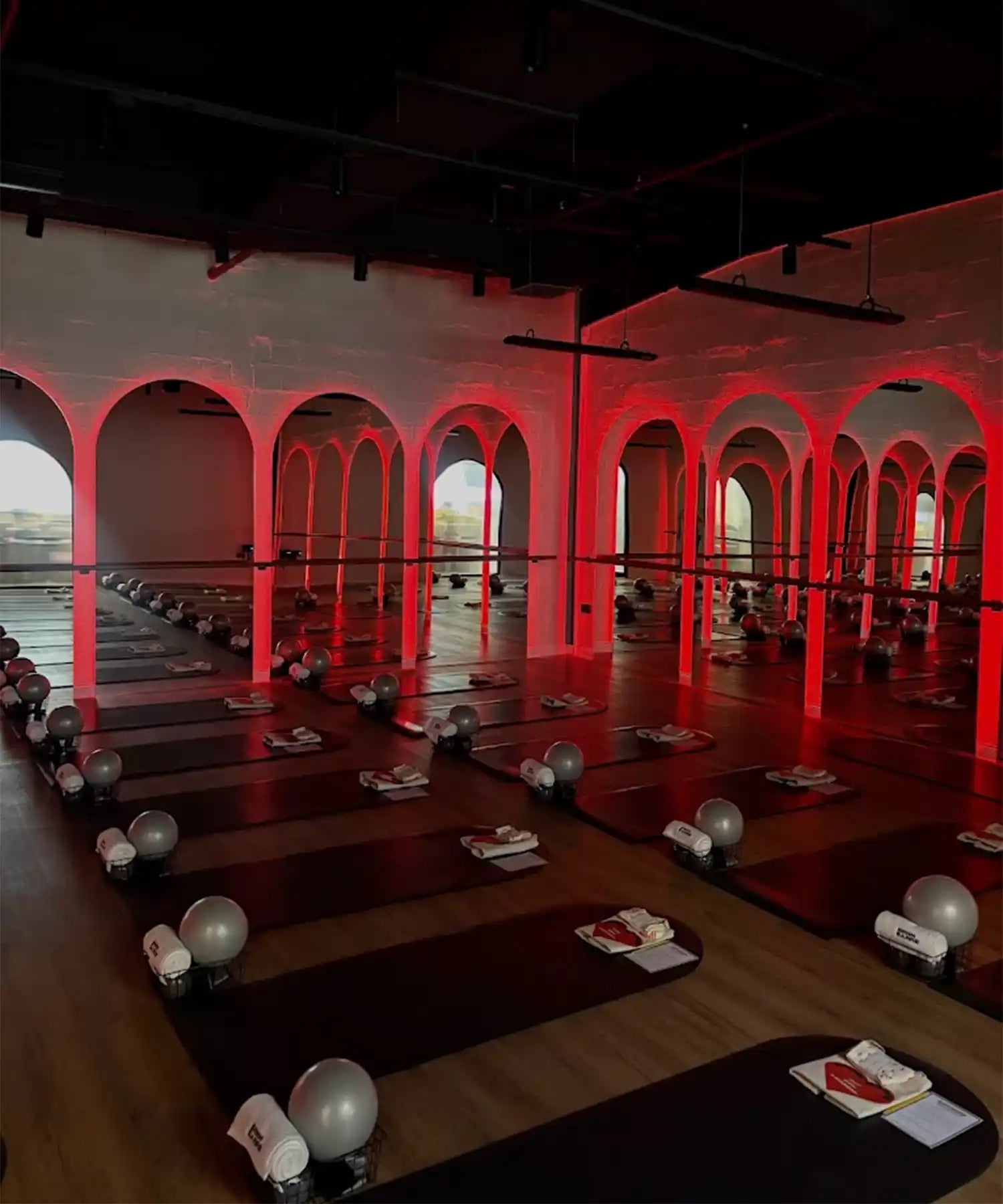 Interior of BRRN BARRE Dubai studio with rows of yoga/barre mats, red-highlighted pillars, overhead IKON infrared heater bars, and a warm-toned environment suited for hot workouts.