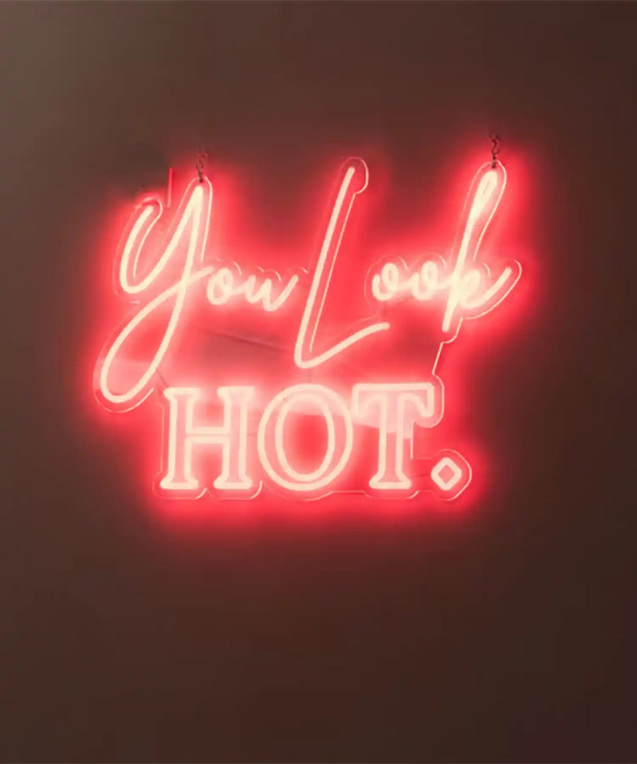 Neon sign reading ‘You Look HOT.’ inside YOURS Studio London, with visible infrared heater bars or panels above, creating a warm studio ambiance.