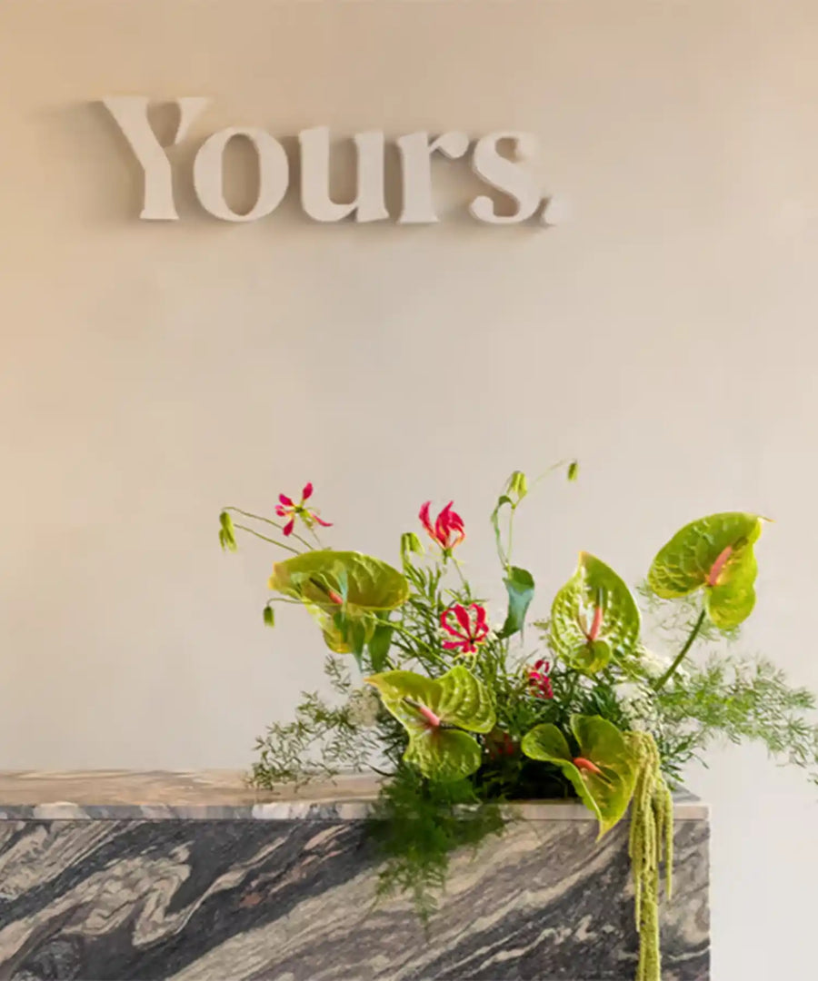 Reception area of YOURS Studio London with marble desk, building signage ‘Yours’, and glimpse of infrared heating installation overhead; modern luxe interior