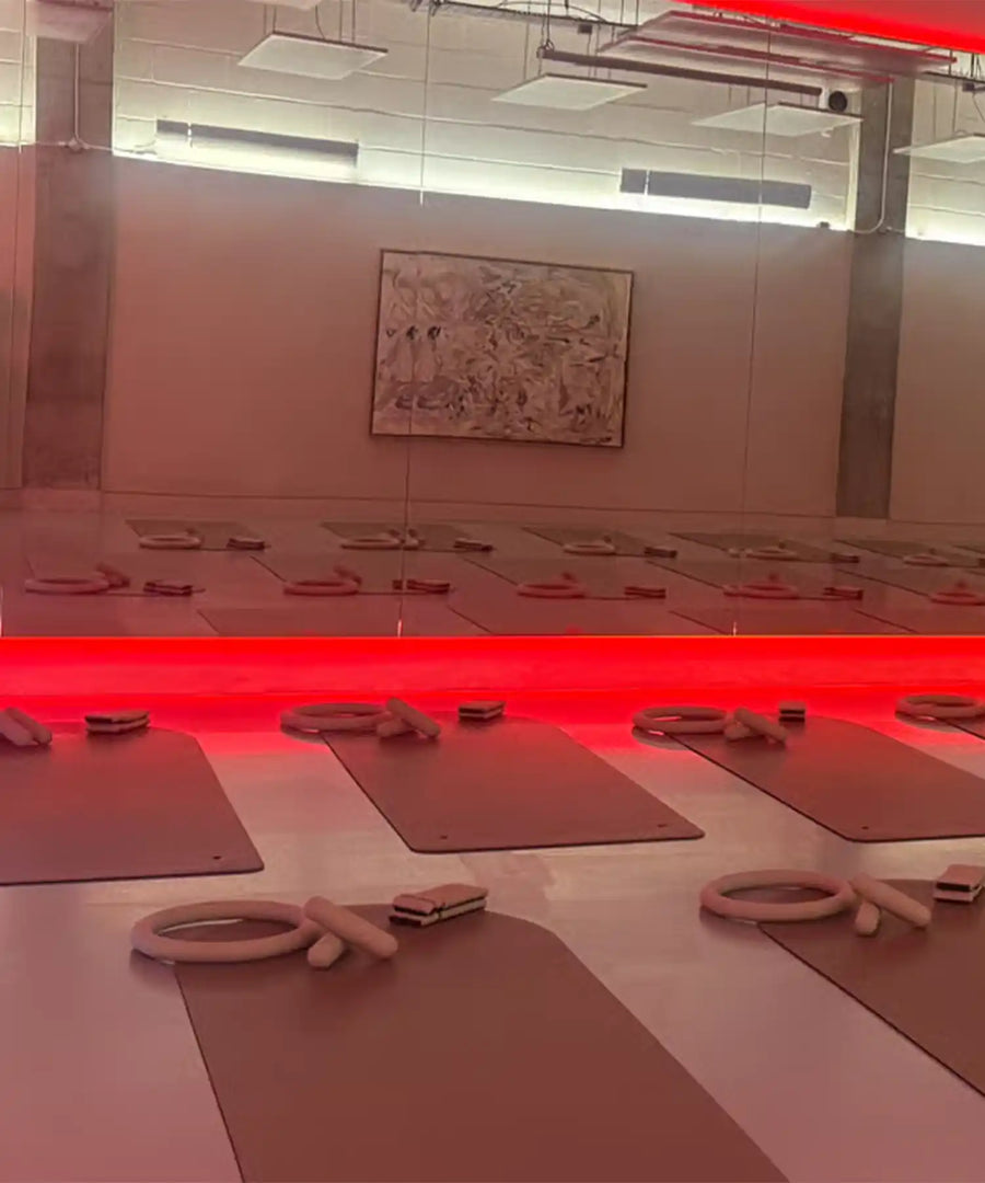 Wide view of YOURS Studio London class zone with hanging infrared heating panels above, neat rows of mats and studio ambient red lighting.