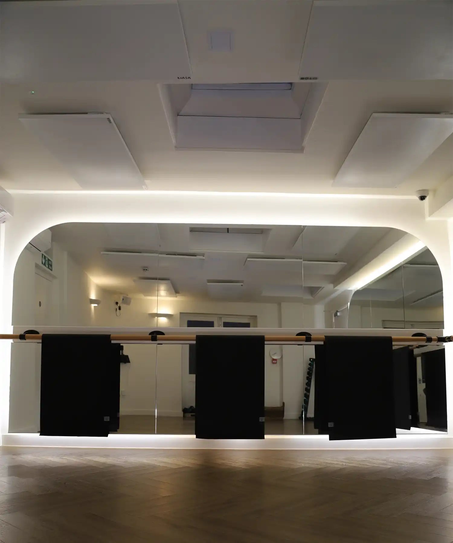 Close-up of black exercise mats hanging from the wooden barre in Reformer Revolution’s mirrored studio, with soft floor lighting and infrared-heated workout space in the background.