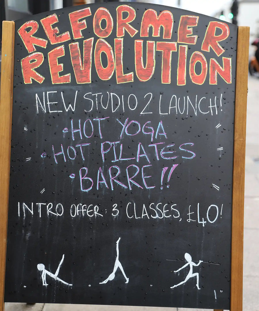 Chalkboard sign outside Reformer Revolution advertising the launch of Studio 2 with Hot Yoga, Hot Pilates and Barre classes, including an intro offer of three classes for £40.