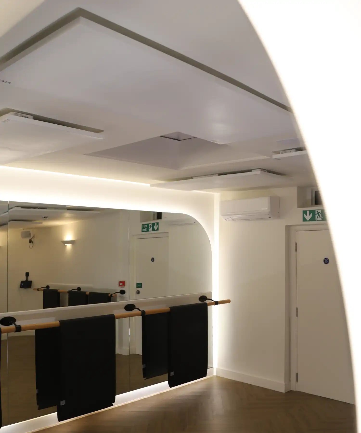 Interior of Reformer Revolution’s barre studio showing wall-mounted mirrors and ballet barres, with KIASA KORE Balance infrared heating panels mounted on the ceiling for hot-studio temperature control.