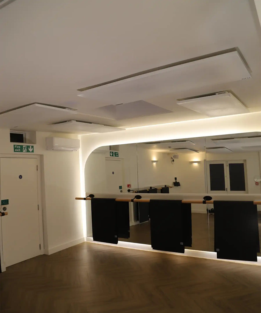 Barre studio interior with ballet barres, mirrored wall and multiple ceiling-mounted infrared heating panels providing full room heat coverage.