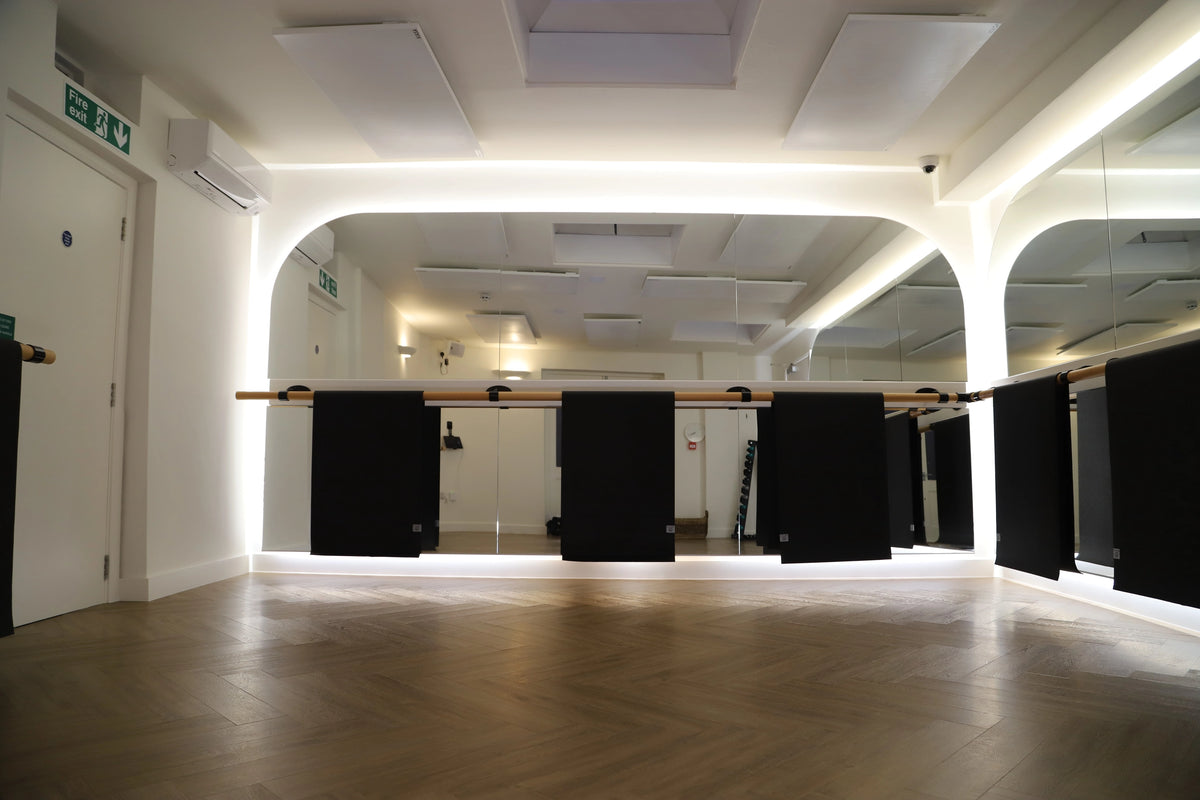 Hot yoga class in warrior pose beneath ceiling-mounted Yoga Balance infrared bars