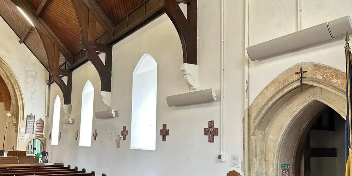 Discrete infrared heater bars mounted below pointed arch windows in a heritage church, installed above wooden pews to provide radiant warmth without altering the historic architecture.